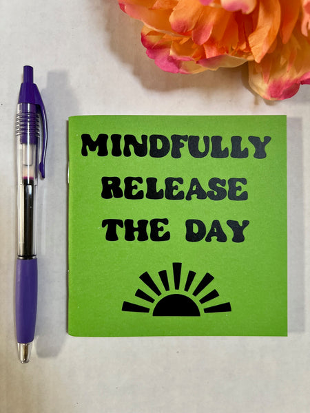 A bright green notepad with the words 'MINDFULLY RELEASE THE DAY' and a black sun graphic
