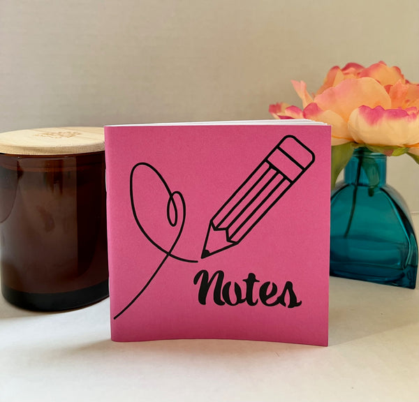 A pink note pad with a black pencil and heart outline and the word 'Notes' printed on the front