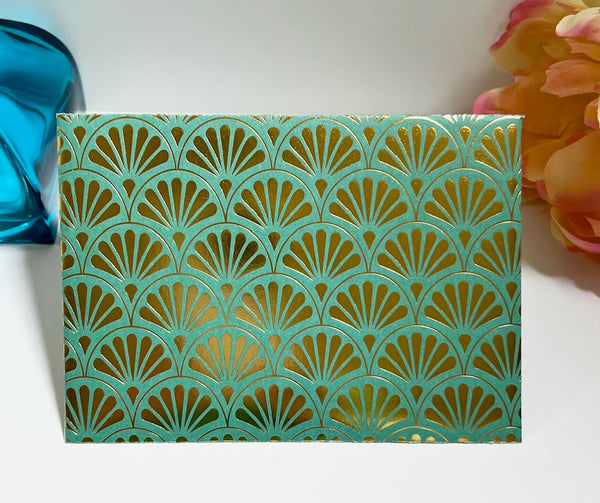 A rectangular decorative envelope featuring a repeating metallic gold fan-shaped cutout pattern over a turquoise background.